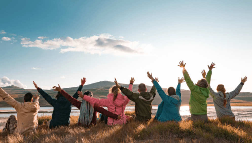 Group raising arms on hilltop overlooking scenic landscape.